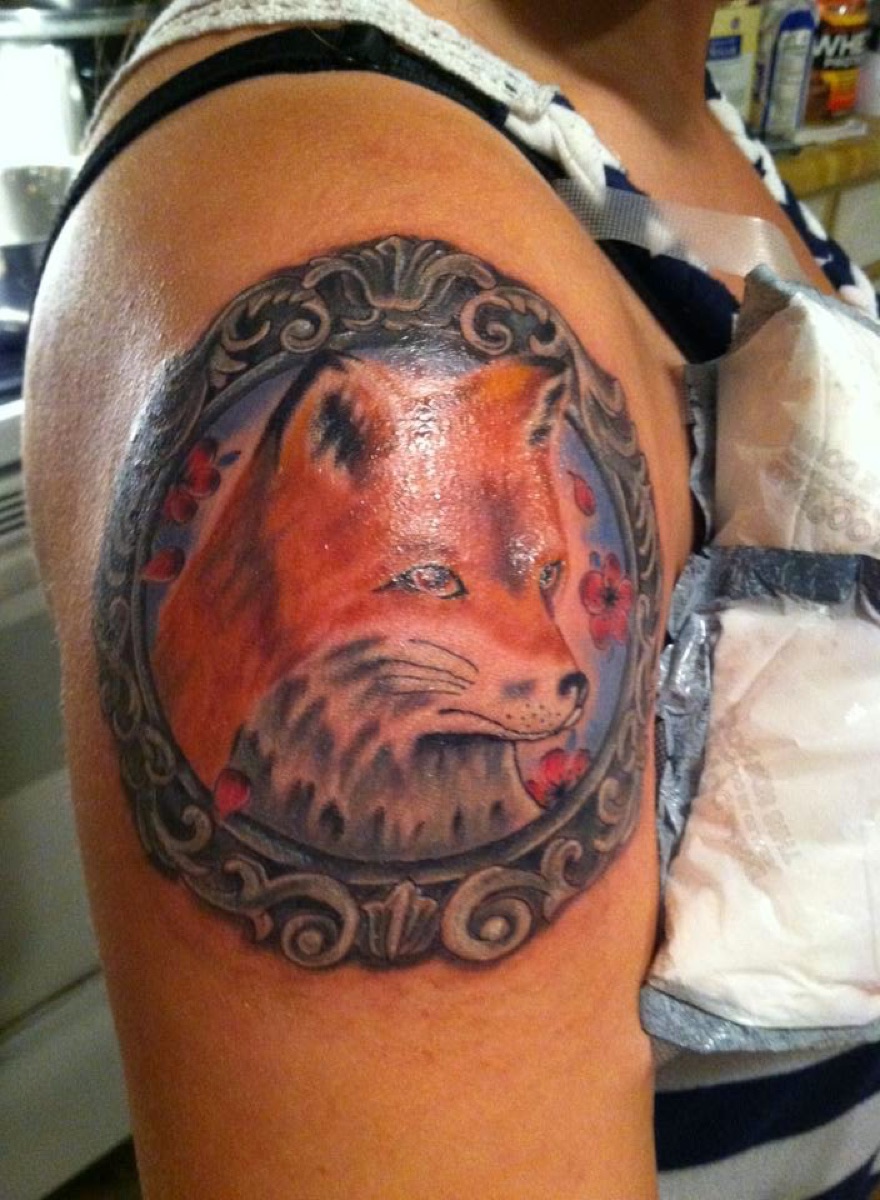 Color fox portrait tattoo inside an ornate frame on the upper arm
