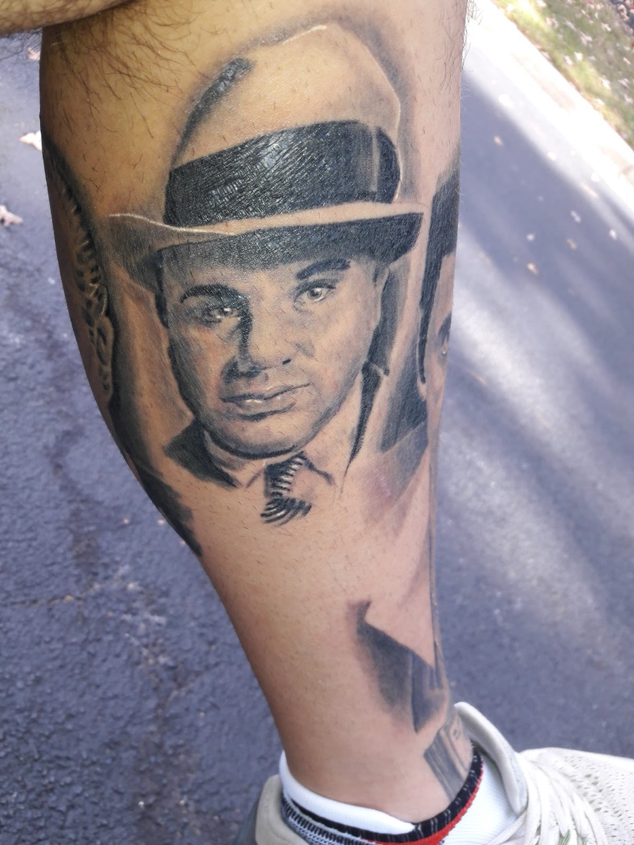 Black and grey realism portrait tattoo of a man in a fedora